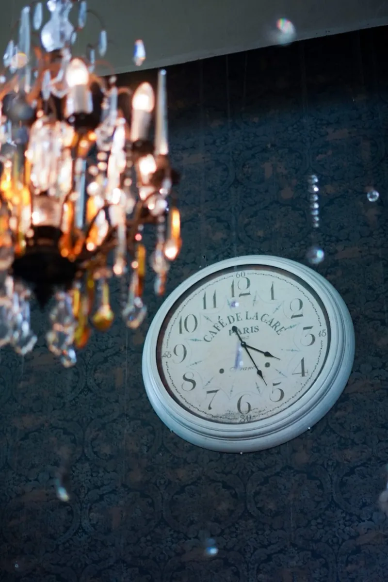 A crystal chandelier beside a wall clock reading Café de la Gare, Paris, hung on dark damask wallpaper