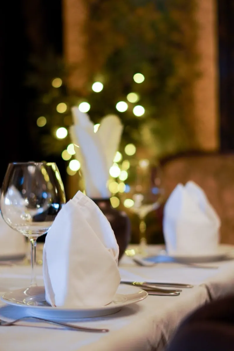A candlelit table setting with folded white napkins and wine glasses, warm lights out of focus behind